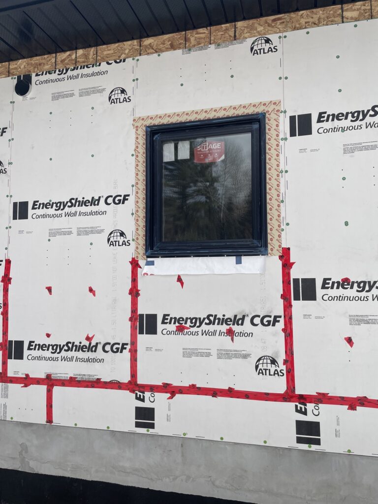 Continuous exterior insulation board with a taped, flashed window opening before siding.