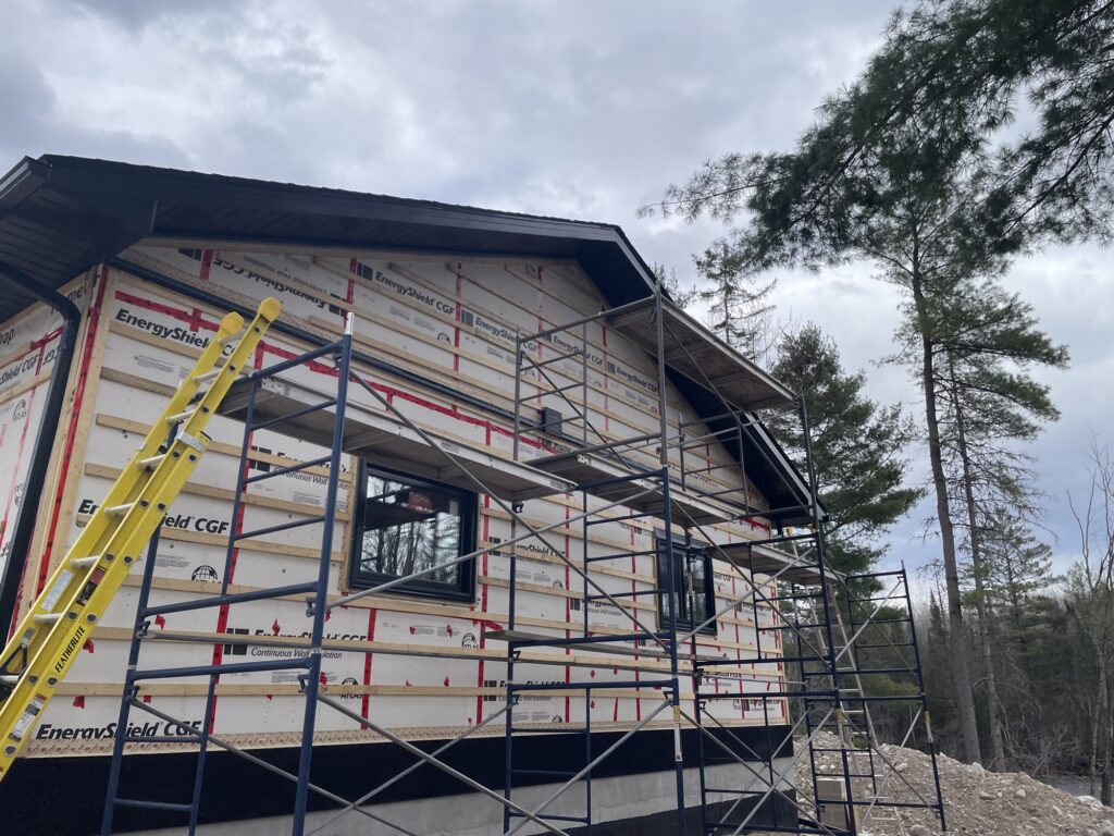 Black vertical metal board-and-batten siding being installed on scaffolding.