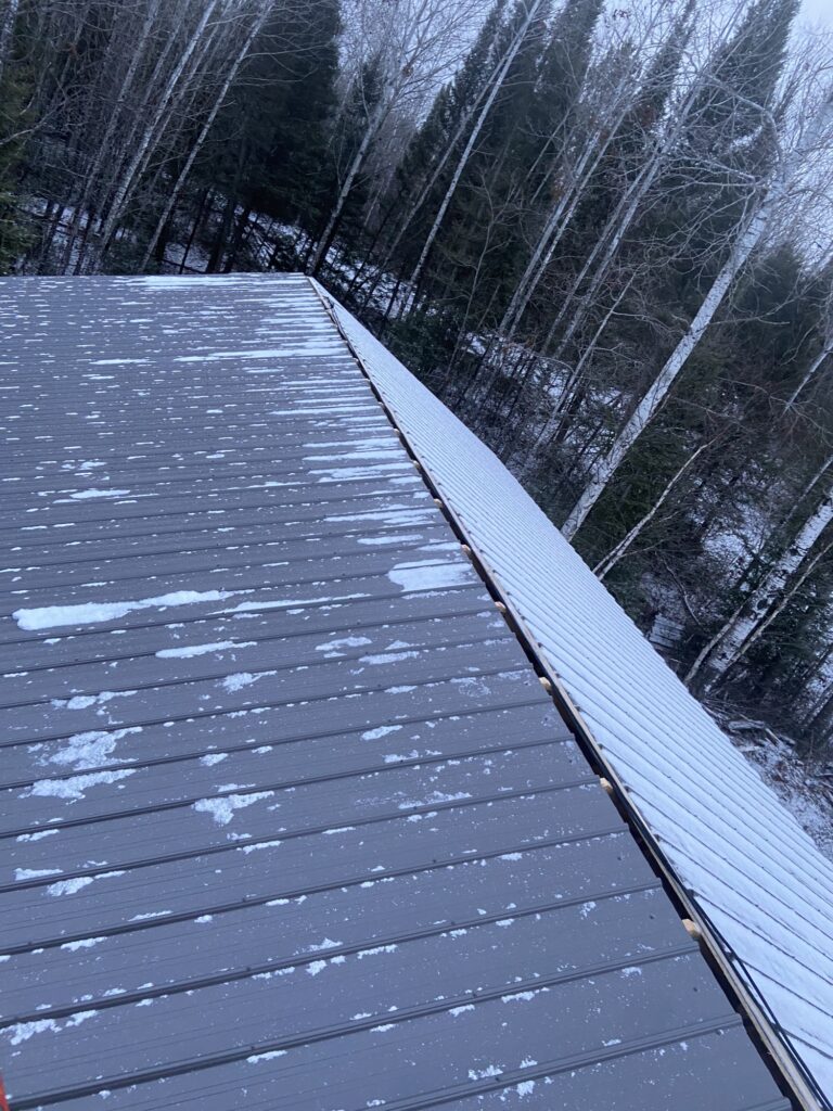 Finished grey metal garage roof dusted with the first snow, forest behind.