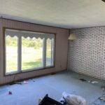 Before renovation — room with pink striped wallpaper, white painted brick wall, drop-tile ceiling and old carpet.