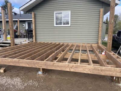 Completed pressure-treated deck joist frame with support posts standing against a green-sided house