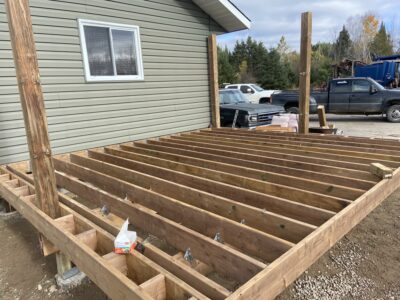 Deck joists fastened with metal hangers and structural screws, with posts rising for a cover