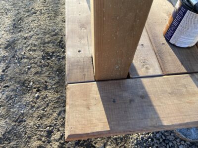 Deck boards around a post being sealed, with a can of wood stain nearby