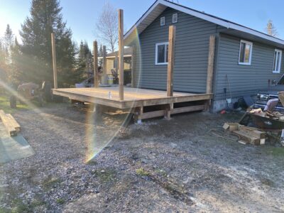 Finished pressure-treated deck platform with support posts against a green-sided home at sunset