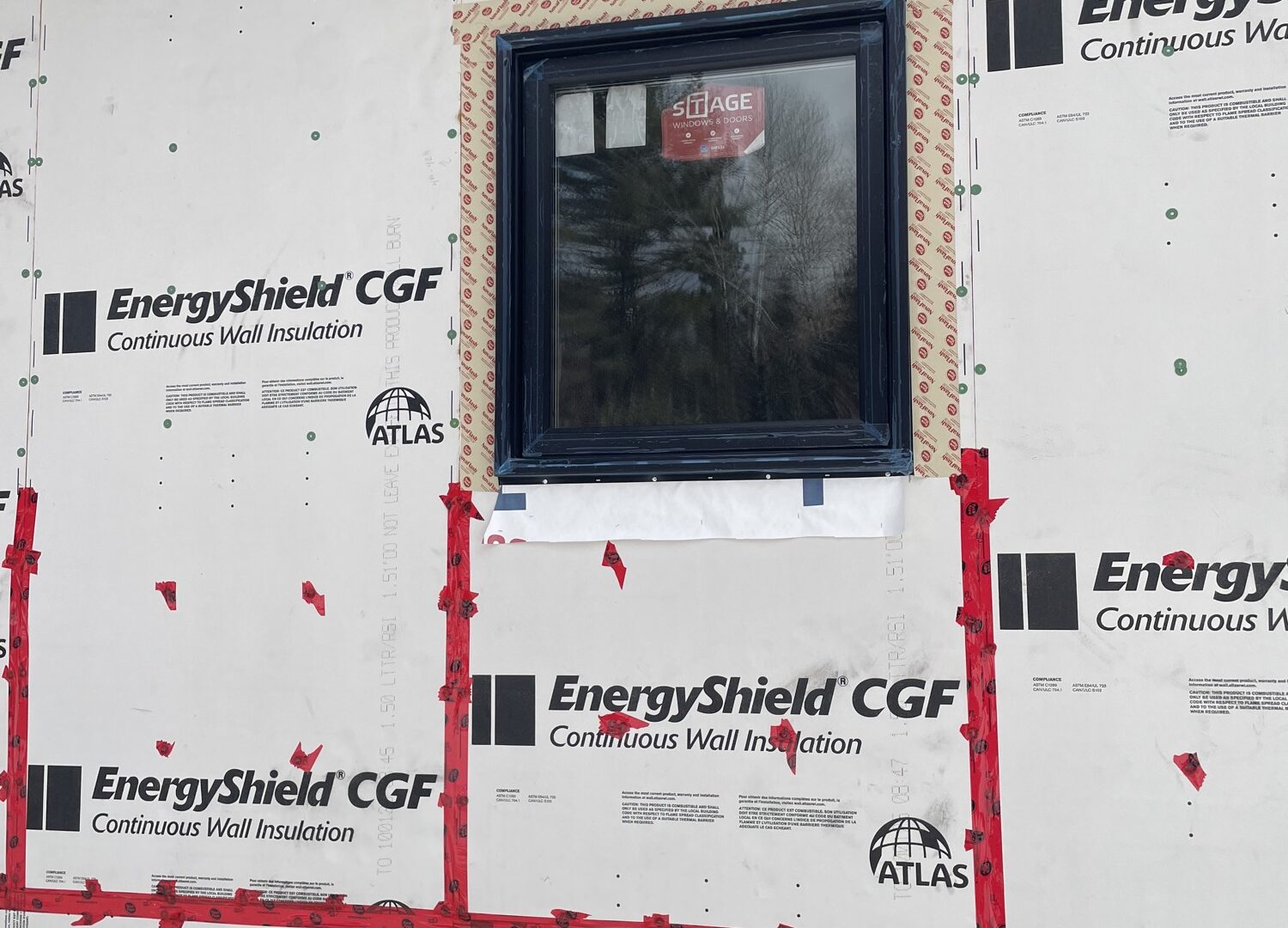 Exterior wall wrapped in taped continuous rigid foam insulation around a new black-framed window