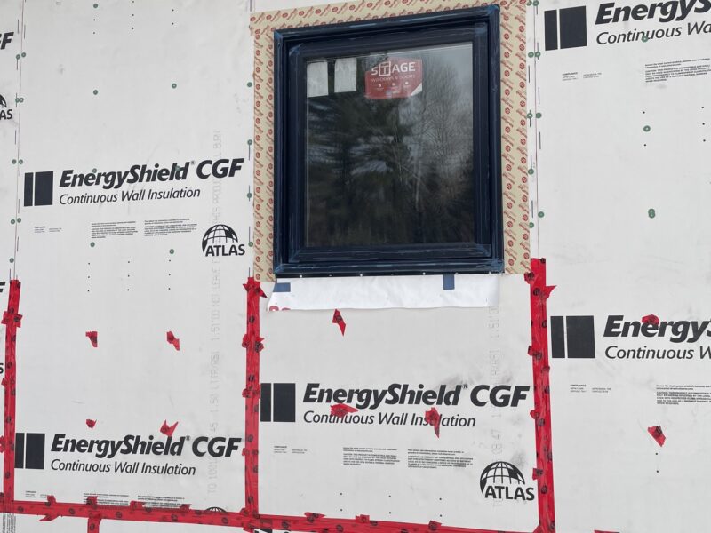 Exterior wall wrapped in taped continuous rigid foam insulation around a new black-framed window