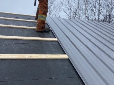 Roofer fastening ribbed steel roofing panels over strapping and underlayment
