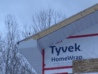 Finished gable eave with white soffit and fascia over house wrap