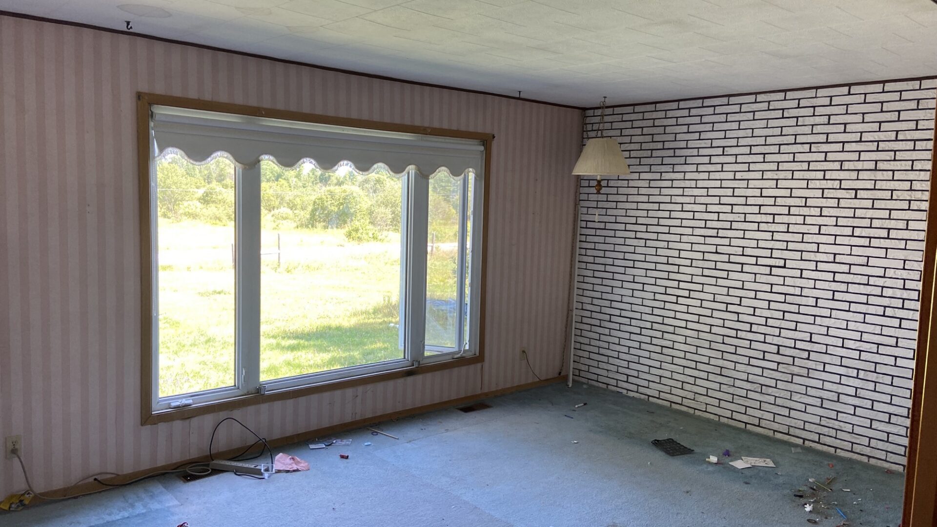 Dated living room before remodel with striped wallpaper, a painted brick wall, and an acoustic-tile ceiling