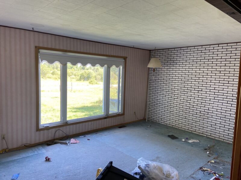 Dated living room before remodel with striped wallpaper, a painted brick wall, and an acoustic-tile ceiling
