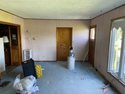 Room before renovation with striped wallpaper, a drop ceiling, and dark wood trim being cleared out