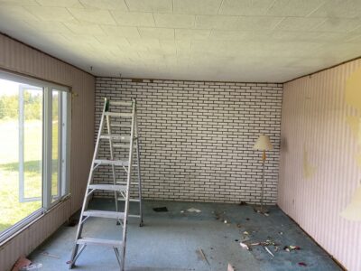 Room mid-demolition with peeling wallpaper and a stepladder beside the painted brick wall