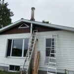 Exterior of the home with a new stainless steel wood-stove chimney installed and ladders in place