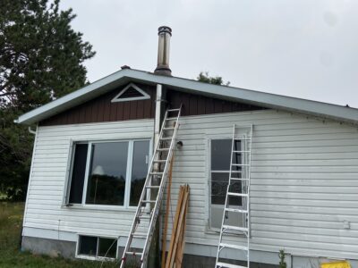 Exterior of the home with a new stainless steel wood-stove chimney installed and ladders in place
