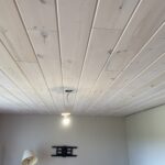 Finished whitewashed plank ceiling with a pendant light and a wall-mounted TV bracket