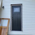 New black craftsman-style exterior door installed in the siding with the old wood door removed