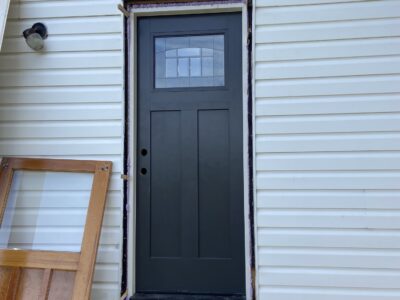New black craftsman-style exterior door installed in the siding with the old wood door removed
