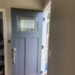 New charcoal craftsman entry door standing open with fresh trim and a plank ceiling above