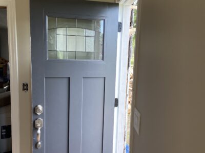 New charcoal craftsman entry door standing open with fresh trim and a plank ceiling above